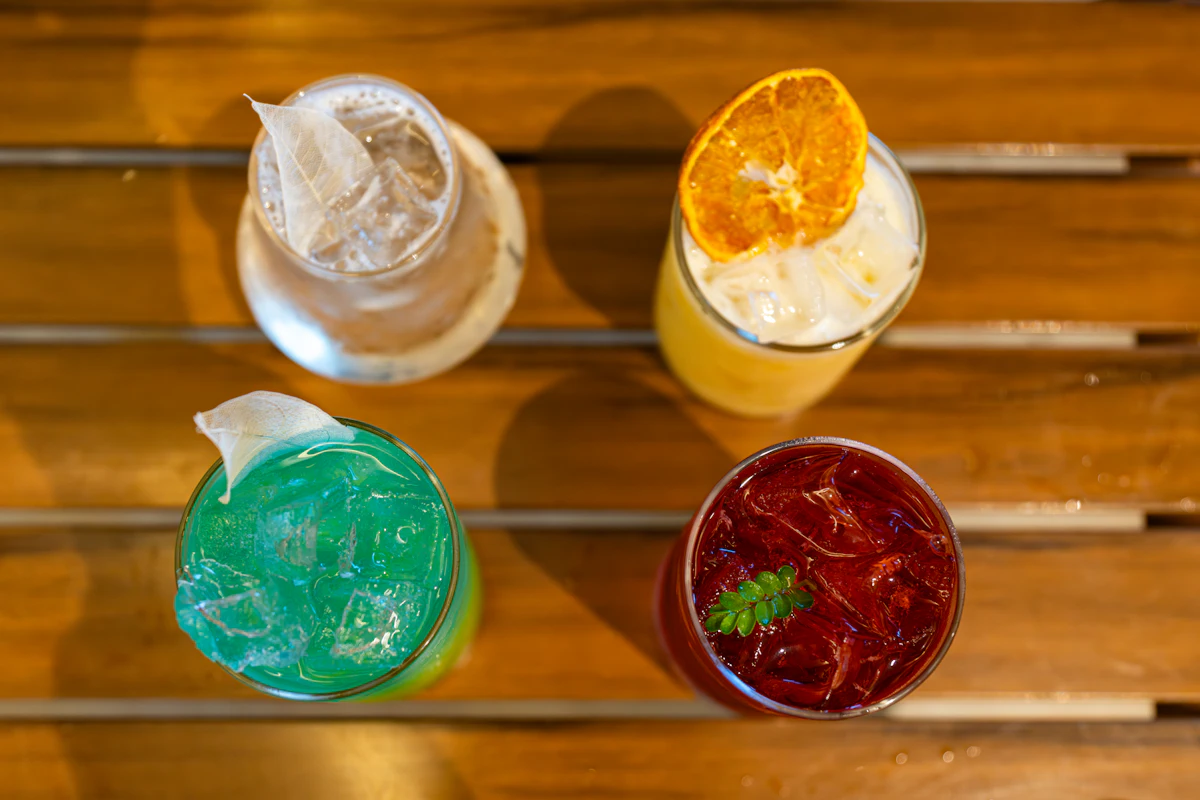 Four brightly coloured drinks in glasses on a wooden table, seen from above