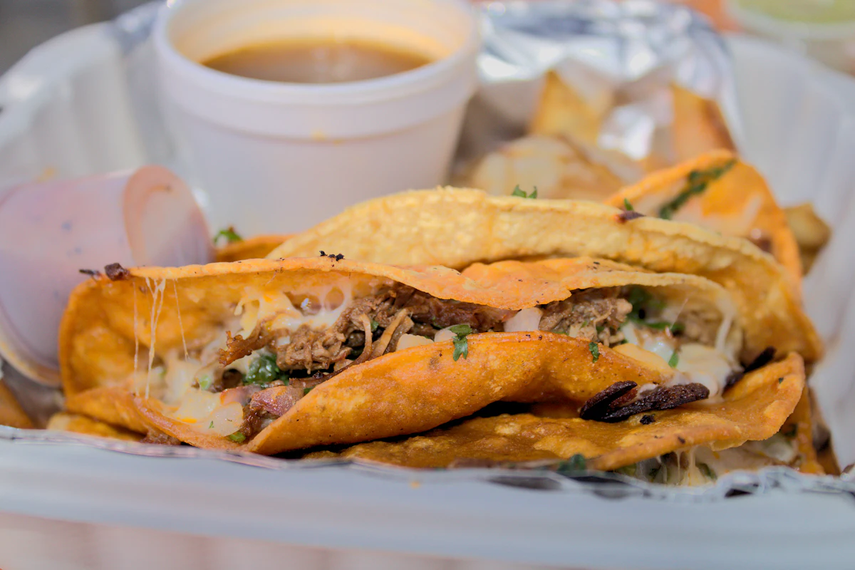 Folded, crisp red tacos with a small bowl of broth for dipping