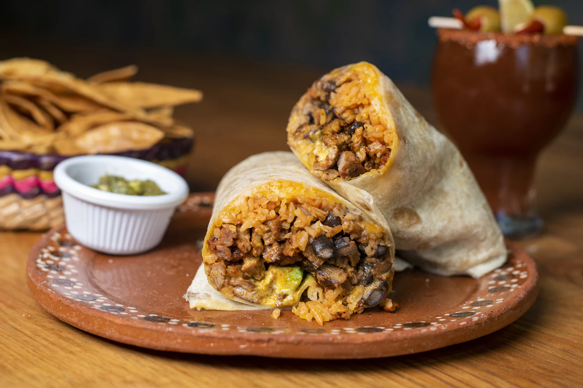 A burrito cut in half to show rice, beans and meat, with a pot of guacamole