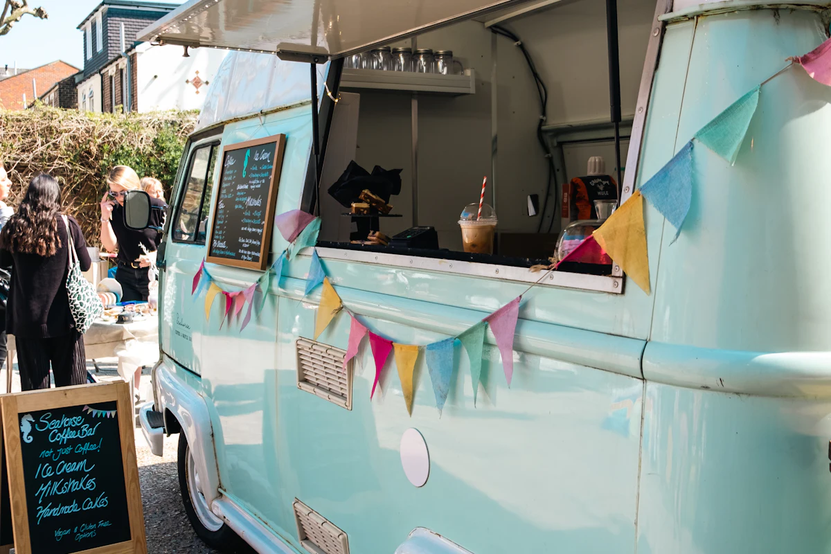 A pale blue food truck decorated with bunting, with a chalkboard menu outside