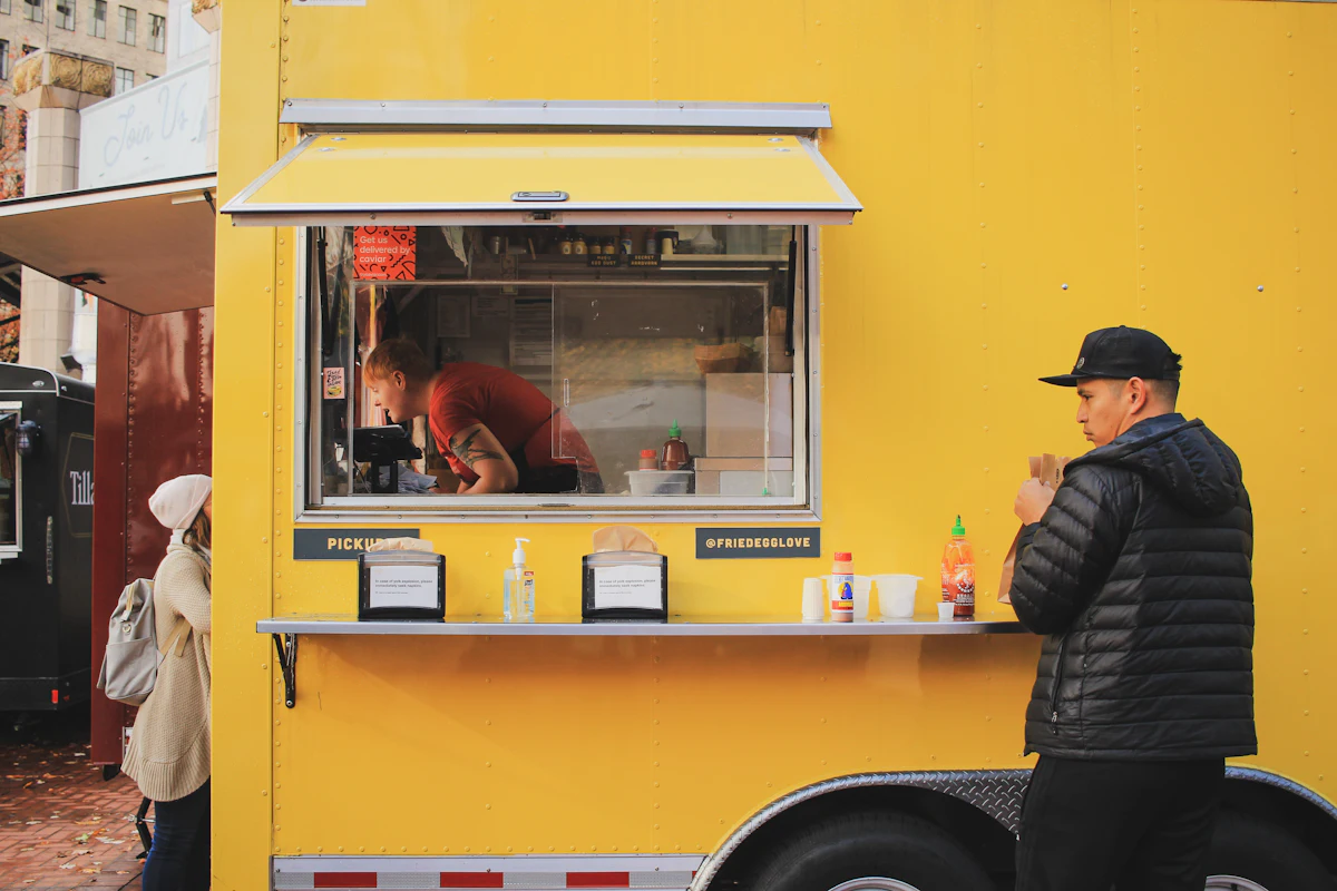 A yellow food truck with its serving hatch open and a customer waiting