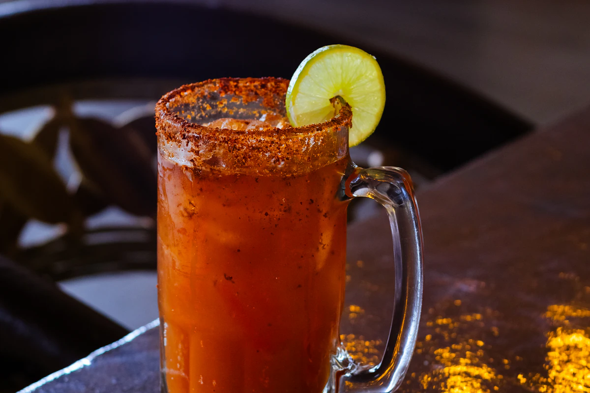 A michelada-style beer drink in a glass with a chilli-salt rim and lime