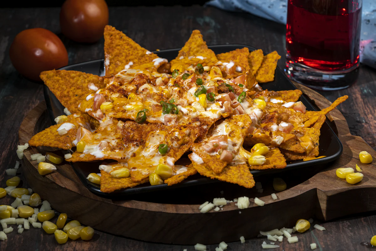 Tortilla chips topped with melted cheese, sweetcorn and sauce on a board