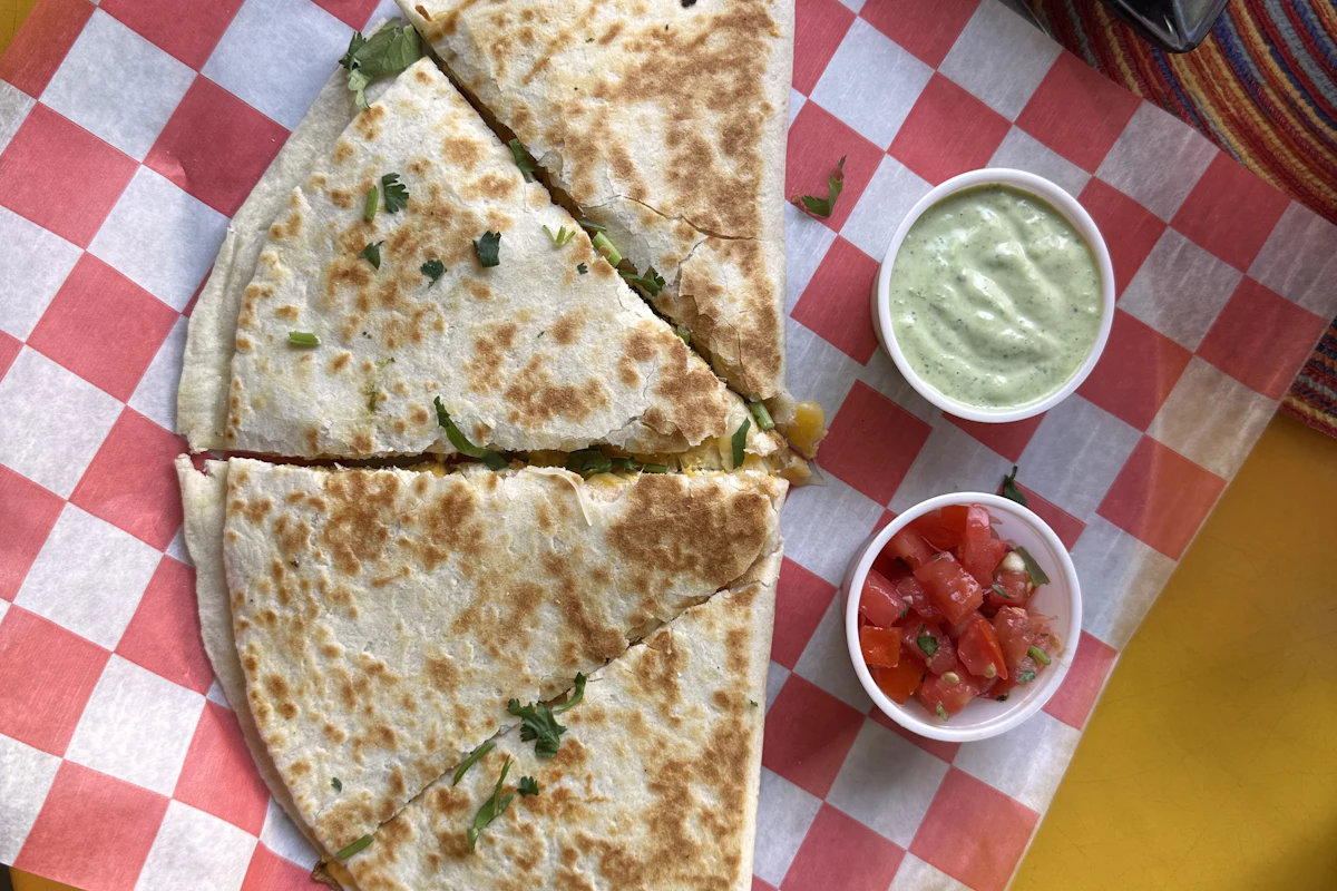 A quesadilla cut into wedges with dips on red and white checked paper