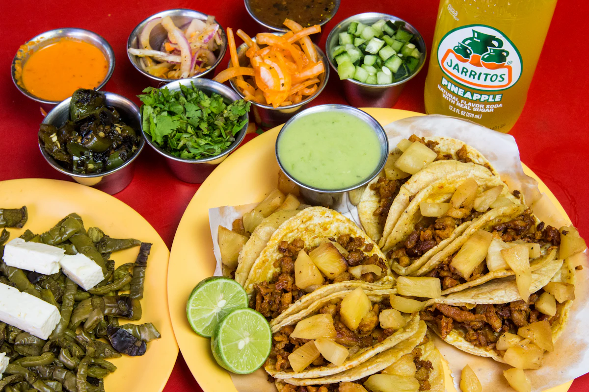 Tacos on a yellow plate surrounded by bowls of salsas, pickles and toppings