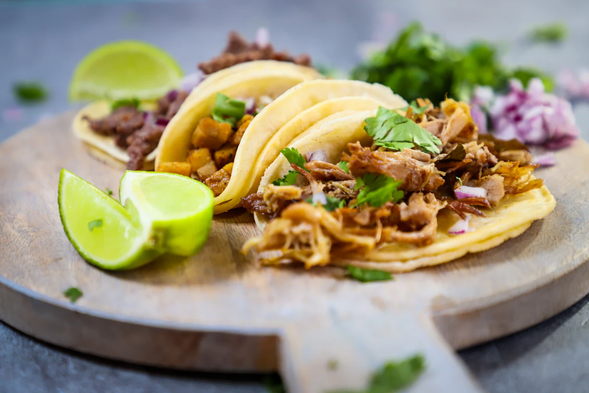 Tacos with shredded meat, lime wedges and coriander on a wooden board